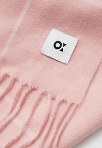 Soft pink scarf made of wool, featuring fringed edges and a small white label with black logo, conveying a smooth texture and simple design.