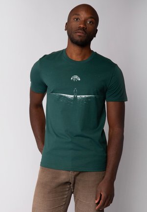 Dark green cotton t-shirt featuring a white graphic of a figure and a landscape with an abstract dome above. Short sleeves, crew neck.