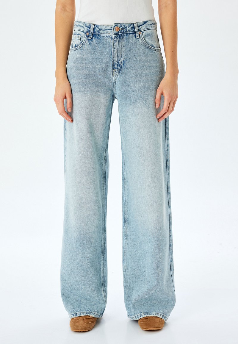 Hellblaue Schlagjeans aus Denim mit hoher Taille, Fünf-Taschen-Design und leichter Ausbleichung, mit sichtbaren Nähten und Messingbeschlägen.