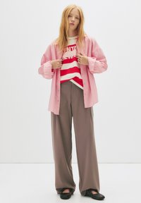 Rosa stribet oversized skjorte lagd over en rød og hvid stribet sweater, parret med brede beige bukser og sorte sko. Simpelt, afslappet look.