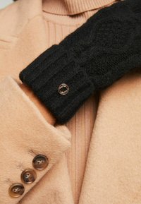 Mustra musta kudum glove, millel on kaablemustrit, ribiga mansett ja metallist aktsent, millele on kombineeritud beez villane mantel nööbiga detailidega.