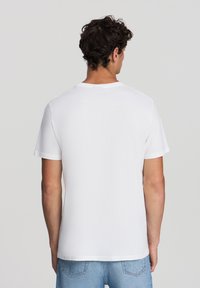 Biała koszulka z krótkim rękawem, wykonana z lekkiej bawełny, z okrągłym dekoltem i gładką fakturą w luźnym kroju.