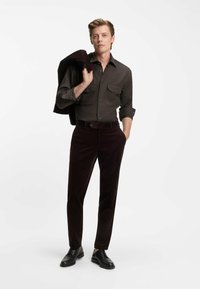 Mørkebrun fløjl bukser parret med en matchende mørk skjorte, begge med en slank pasform. Sorte sko fuldender outfittet.