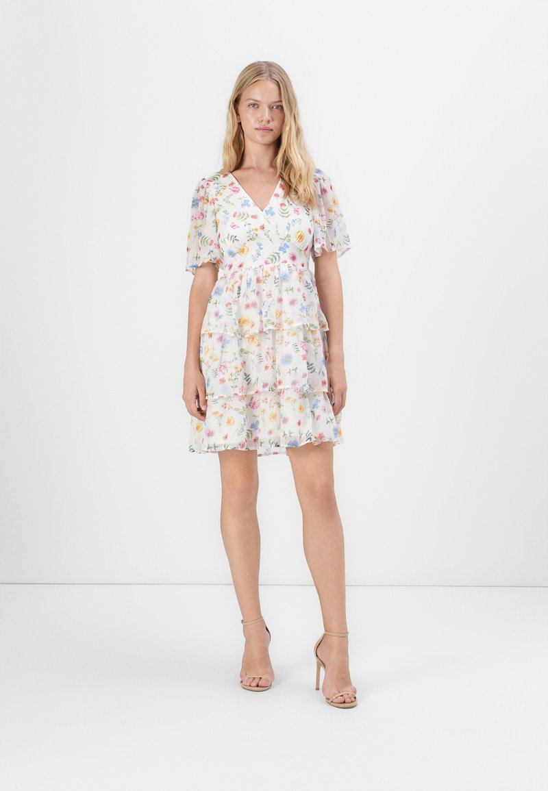 Robe à manches courtes imprimée de motifs floraux, avec un décolleté en V, des volants et un tissu léger et transparent dans des teintes pastel.