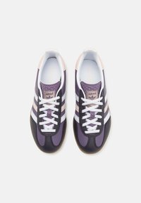 Buty sportowe na sznurowadła w kolorach czarnym, fioletowym i jasnoróżowym. Posiadają trzy białe paski, fakturowaną cholewkę i gumową podeszwę.