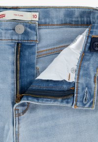 Ljusblå denimjeans med dragkedja och knappstängning, med kontrasterande gul sömnad och en etikett som läser "726 FLARE" storlek 10.