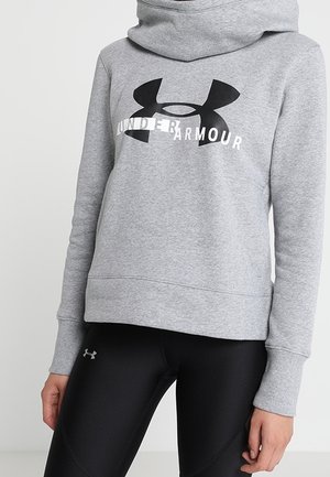 Grijze Under Armour hoodie met groot zwart logo en tekst, gedragen met zwarte Under Armour leggings, waarbij torso en armen zichtbaar zijn.