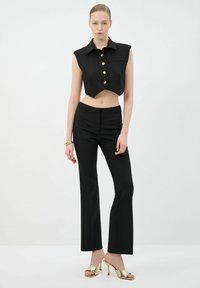 Black cropped sleeveless top with gold buttons, paired with fitted black pants and metallic high-heeled sandals, smooth texture throughout.
