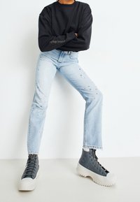 Ljusblåjeans med paljetter, kombinerat med mörkgrå hög-top sneakers och en svart långärmad sweatshirt.