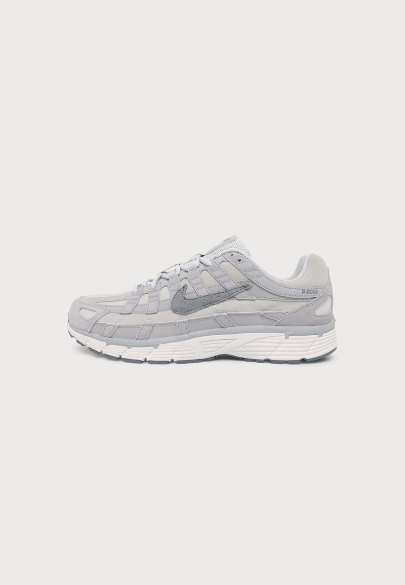 Ανοιχτό γκρι αθλητικό παπούτσι Nike P-6000 με επάνω μέρος από σουέτ και δίχτυ, σκούρο γκρι λογότυπο swoosh, λευκή σόλα και σχέδιο με κορδόνια, εμφανίζεται από το πλάι σε λευκό φόντο.