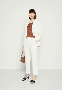 Blazer e calças brancas ajustados, combinados com um top de satin castanho. Saltos pretos de tiras. Bolsa castanha com design minimalista.