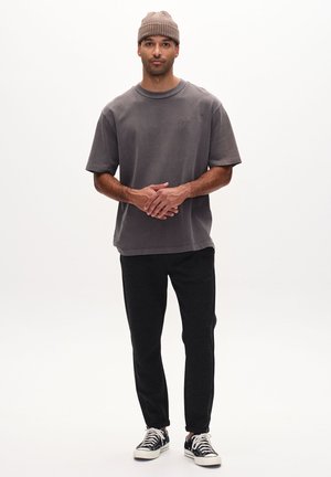 Grau oversized T-Shirt aus weichem Baumwollstoff, kombiniert mit schwarzen strukturierten Jogginghosen und schwarz-weißen Sneakern. Das Modell trägt eine beige Mütze.