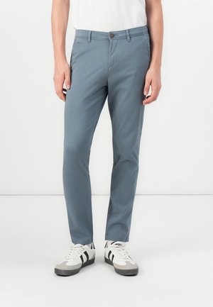 Chinos celestes de mezcla de algodón, con un corte ajustado, cierre de botón y bolsillos laterales, combinados con zapatos blancos con rayas negras.