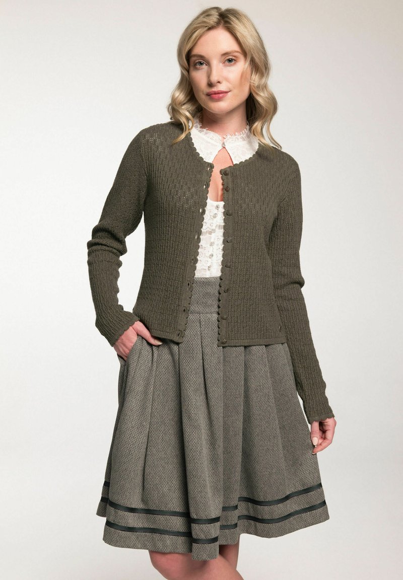 Cardigan en tricot vert olive avec texture côtelée et fermeture à boutons, associé à une jupe grise présentant un subtil motif en chevrons et des rayures noires.