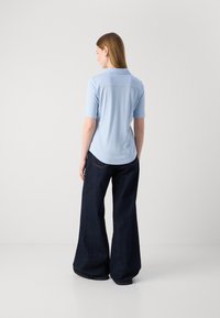 Polo bleu clair à manches courtes avec un col, associé à un jean en denim foncé à jambes larges. Texture lisse et coupe décontractée.