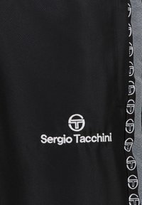 Schwarze Sportshorts aus strukturiertem Material. Verfügt über ein weißes "Sergio Tacchini"-Logo und einen gemusterten Saum entlang der Seiten.