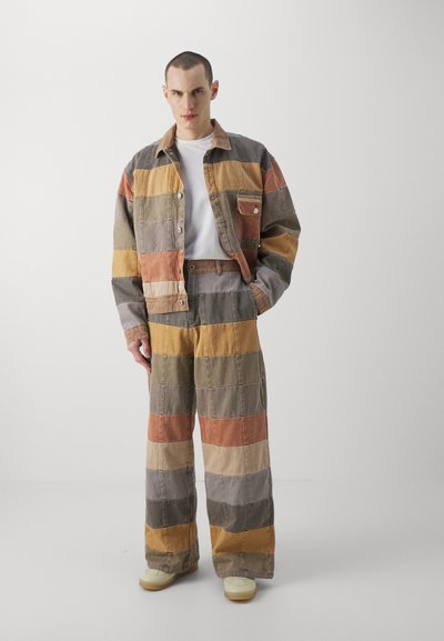 Gestreifte Jeansjacke und weit geschnittene Hose in erdigen Tönen von Orange, Grau, Oliv und Gelb. Mit Taschen und einem lockeren Schnitt.