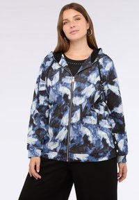 Giacca con cappuccio caratterizzata da un motivo astratto blu e bianco su sfondo nero, con zip frontale e dettagli con bottoni laterali.
