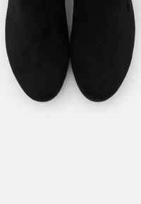 Bottes noires en daim jusqu'à la cheville avec un bout arrondi et une texture lisse, présentant un design sans couture et sans matériel ni accents visibles.