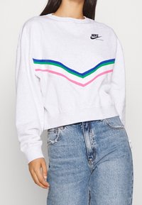 Kratká mikina Nike ve světle šedé barvě s chevronovým designem v modré, zelené, růžové a bílé barvě napříč hrudí. Směs bavlny.