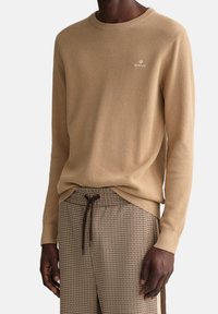 Pull en tricot beige avec col rond et motif texturé, associé à un pantalon marron à motif pied-de-poule avec taille à cordon.