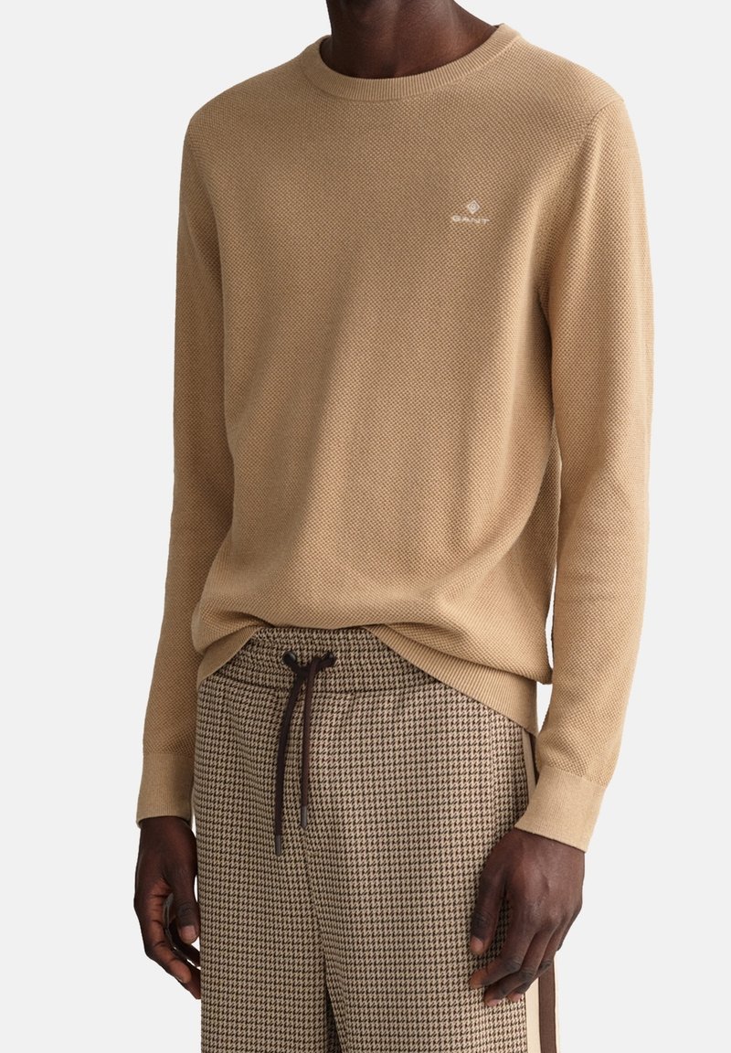 Pull en tricot beige avec col rond et motif texturé, associé à un pantalon marron à motif pied-de-poule avec taille à cordon.