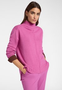 Maglione rosa a collo alto con polsini e orlo a coste, caratterizzato da spacchi laterali e una finitura testurizzata, abbinato a pantaloni rosa coordinati.