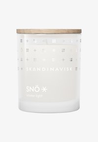 Bougie blanche étiquetée "SNÖ Lumière d'hiver" dans un support en verre transparent avec des motifs croisés en argent et un couvercle en bois sur le dessus.