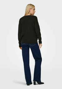 Maglione nero lavorato a maglia con scollatura ampia, abbinato a jeans dritti blu scuro. Il modello indossa stivali neri con tacco alla caviglia.