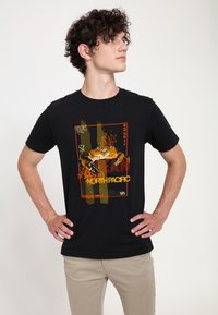 Sorte bomulds t-shirt med et farverigt krabbe grafik med teksten "NORTH PACIFIC" i gul og rød, mod en tekstureret baggrundsdesign.