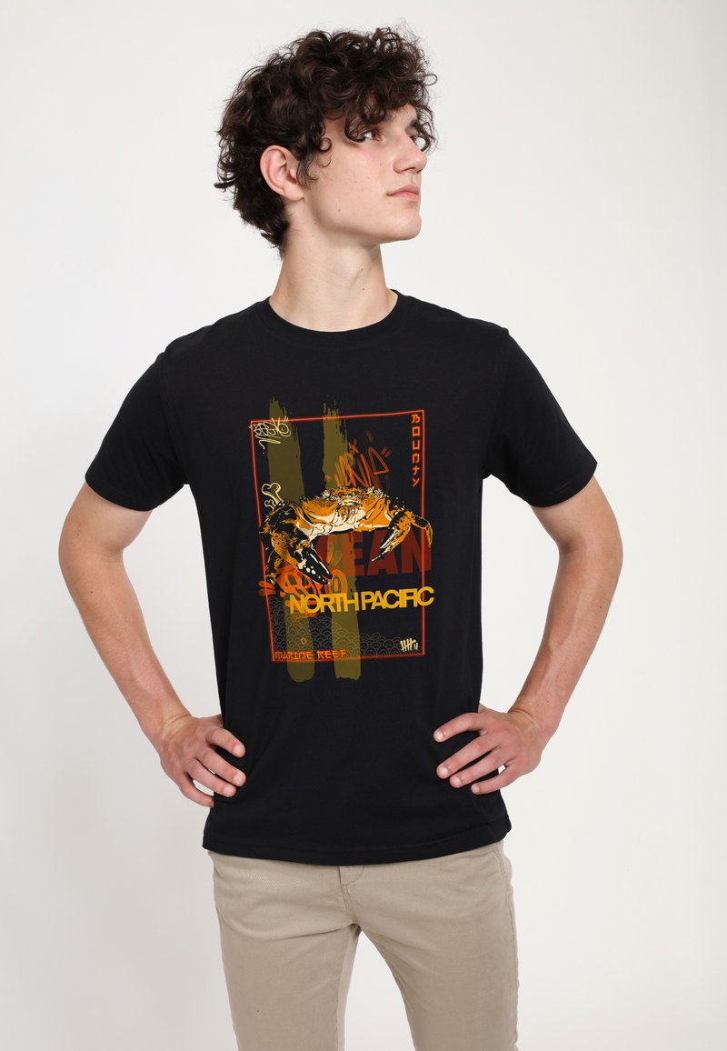 Sorte bomulds t-shirt med et farverigt krabbe grafik med teksten "NORTH PACIFIC" i gul og rød, mod en tekstureret baggrundsdesign.