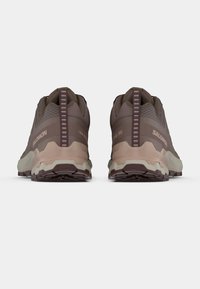 Καφέ παπούτσια για τρέξιμο σε μονοπάτια με πάνελ από δίχτυ, υφασμένα επικάλυψης και παχιά λαστιχένια σόλα. Το πίσω μέρος διαθέτει θηλιά για τράβηγμα και αντίθετες λεπτομέρειες.