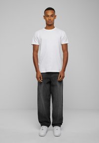 White crew-neck t-shirt paired with loose-fitting black jeans and white sneakers. The fabric appears smooth, and the jeans have a dark wash.