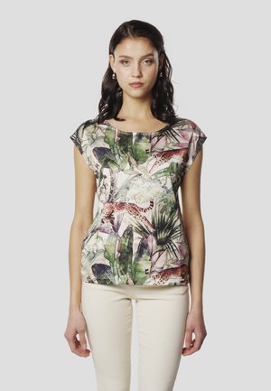 Majica s kratkimi rokavi s pisanim rastlinskim in živalskim vzorcem na svetli tkanini, ohlapnega kroja z okroglim izrezom. Združena z bež hlačami.