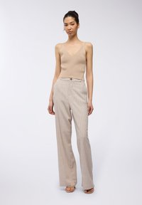 Top in cotone beige a costine con scollatura a V, abbinato a pantaloni wide-leg beige chiaro con righe e dettaglio con bottone. Tessuti con texture liscia.