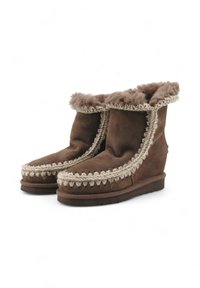 Stivaletti alla caviglia in suede marrone con fodera in pelliccia sintetica, rifiniture decorative intrecciate e suola piatta. Il design presenta un risvolto in alto.