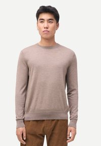 Beiger Langarm-Pullover aus leichtem, weichem Strick mit Rundhalsausschnitt und gerippten Bündchen. Kombiniert mit braunen Cordhosen.
