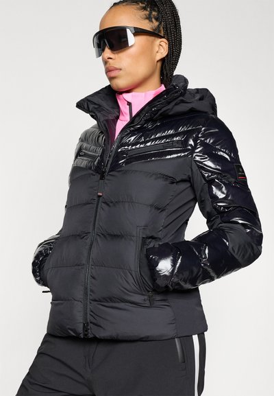 Μαύρο μπουφάν με γυαλιστερή φινίρισμα, κλείσιμο με φ�ερμουάρ, κουκούλα, πλευρικές τσέπες και οριζόντια ραφή; φορεμένο πάνω από ροζ μπλούζα.