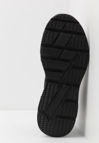 Semelle de chaussure de sport noire avec une surface texturée à motifs multiples pour une meilleure adhérence ; comporte des sections distinctes et un design géométrique en relief.