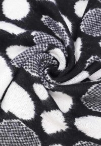 Tessuto a fantasia bianco e nero, con grandi pois e un motivo houndstooth, dalla texture morbida e dalla forma flessibile e intrecciata.