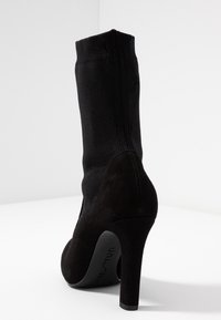Botín negro de tacón alto con parte superior de tejido tipo calcetín y tacón de ante, con un acabado suave y una textura sutil.