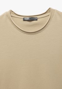 Beige slim-fit t-paita, jossa on pyöreä kaula-aukko ja joka on valmistettu pehmeästä puuvillakankaasta. Näkyvissä olevan tuotemerkin ja koon hintalappu. Sujuva pinta.