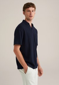 Cămașă bleumarin cu mânecă scurtă, cu un model texturat, guler cu tăietură și un buzunar pe pieptul stâng, asortată cu pantaloni de culoare deschisă.