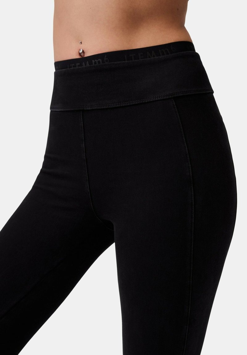 Primo piano di una persona che indossa leggings neri a vita alta con un cinturino piegato e un piercing visibile all'ombelico.