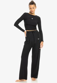 Black ribbed long-sleeve crop top with a round neckline paired with loose black pants. Features a drawstring waist and small logo detail.