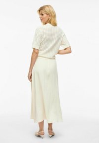 Haut en tricot crème à manches courtes avec une texture à motifs, associé à une jupe midi fluide crème et des sandales à talons de couleur claire.