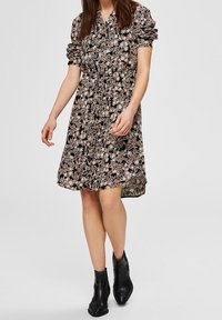 Svart blommig klänning med korta puffärmar, en krage och en löst sittande passform. Tyget har ett mönster av små vita och rosa blommor.