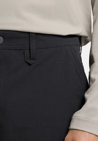 Zwarte broek van een gestructureerde stof, met een platte voorkant, zijzakken en een knoopsluiting, gecombineerd met een lichtbeige top.