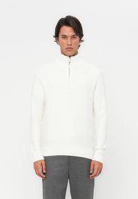 White knit sweater with a high collar and half-zip closure. Features ribbed cuffs and waistband. Smooth texture, minimalistic design.