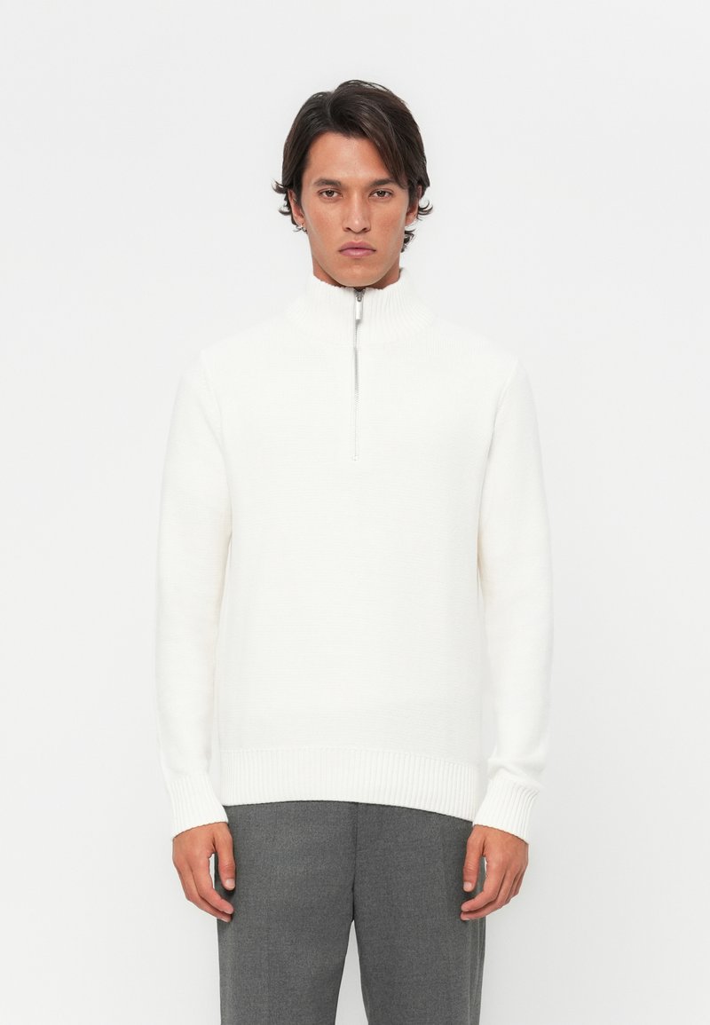 White knit sweater with a high collar and half-zip closure. Features ribbed cuffs and waistband. Smooth texture, minimalistic design.